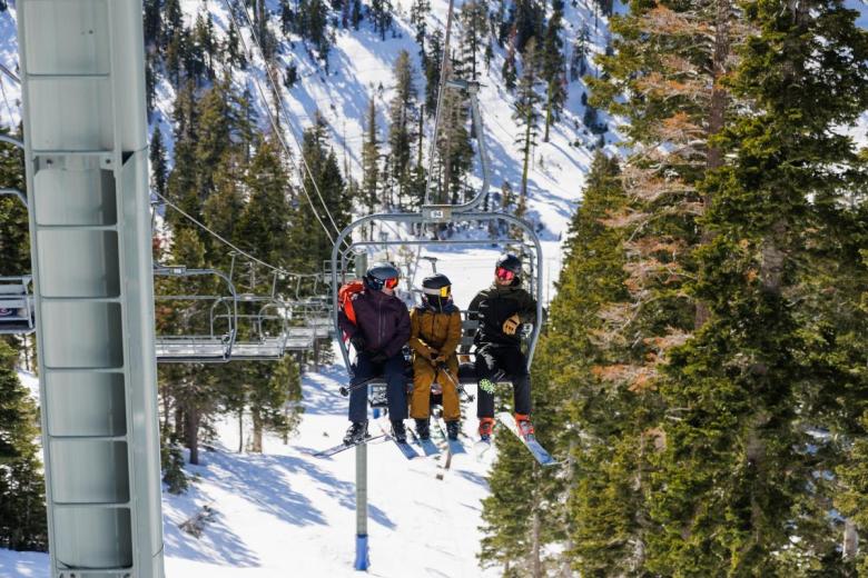 Three skiers ride up a chair lift on a sunny day at the resort