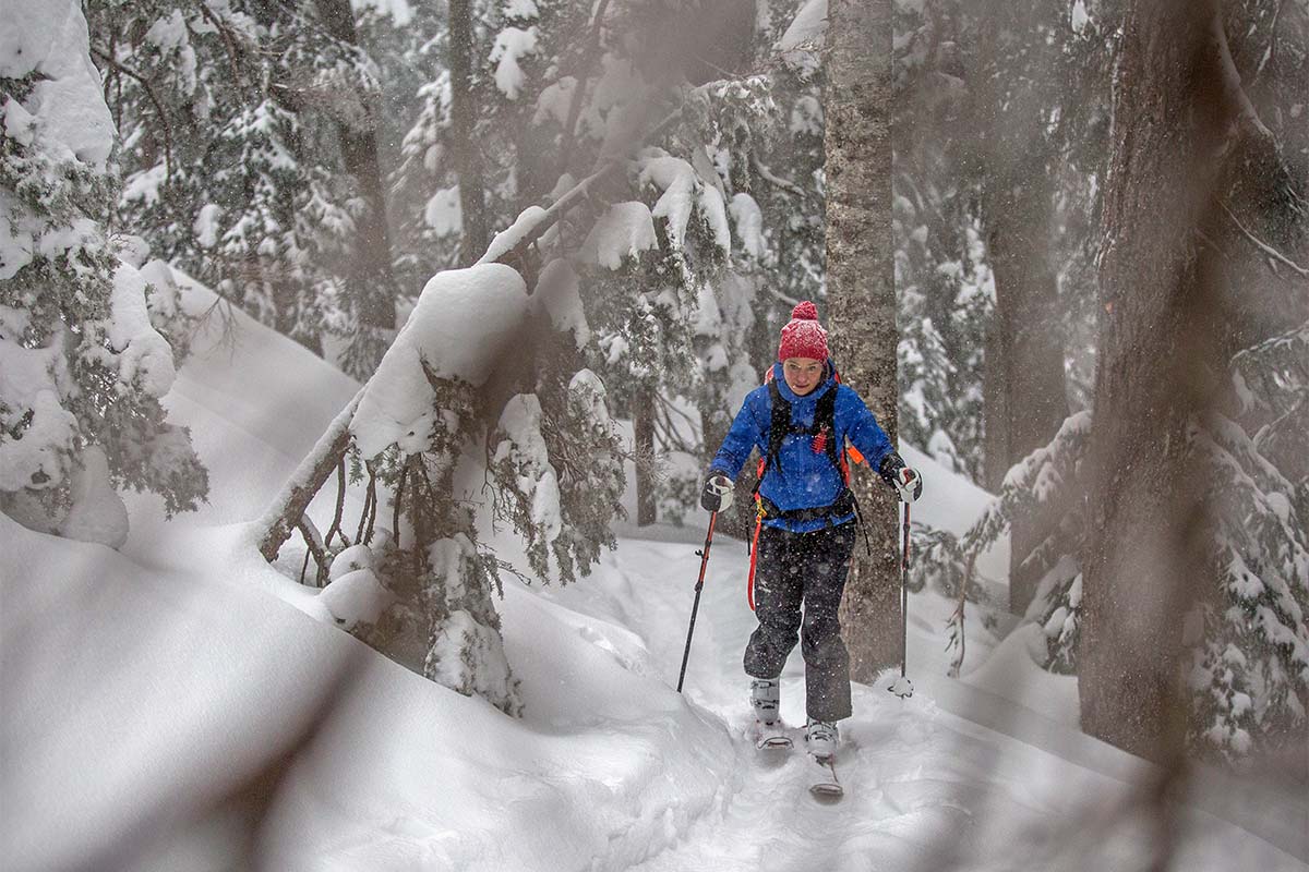 A woman with a backpack ski tours through an area dense with trees