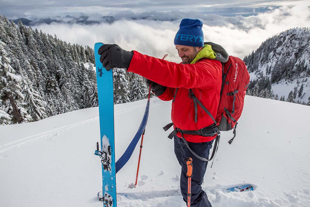 A man in a bright red jacket pulls the skin off a ski