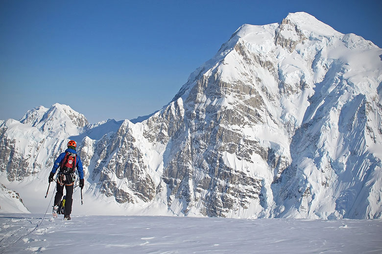 A climber treks to a high, snow-covered peak in mountaineering boots. 