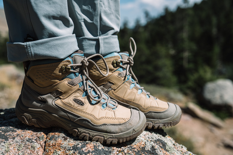 A close up of a pair of brown leather hiking boots standing on a granite rock