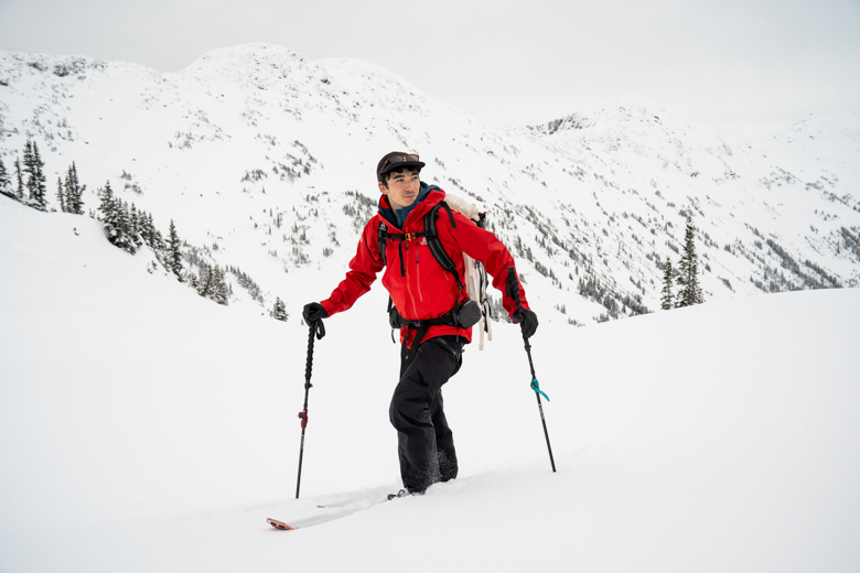 A man backcountry skiing in a red hardshell jacket