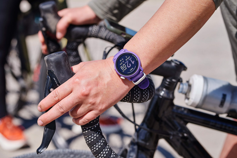 A purple GPS watch on a wrist holding onto bike handlebars