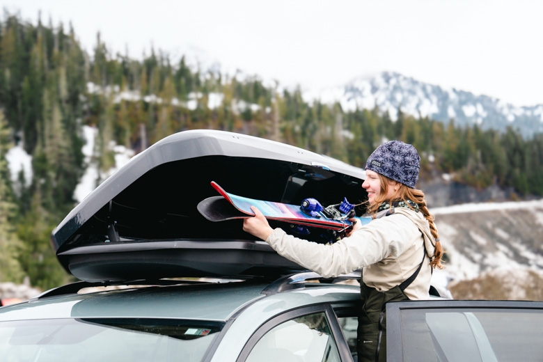 A woman puts a pair of skis inside a black cargo box