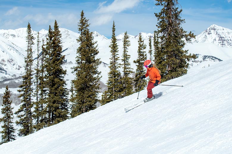 A skier turns down a slope on a sunny day in the mountains.