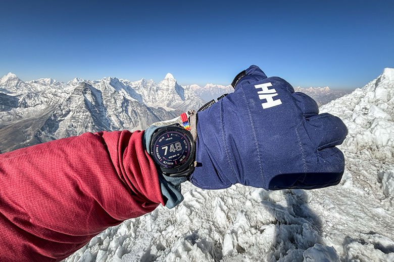 A closeup of a wrist with the Garmin Fenix 7 with snowy mountain peaks in the background