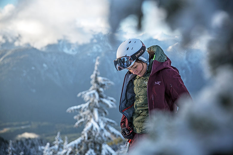 A woman skiing in the wintry backcountry zips layers up to keep warm. 
