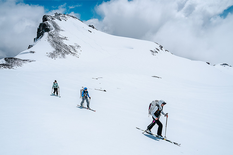 A group of skiiers climb a steep, snowy peak in the mountains.