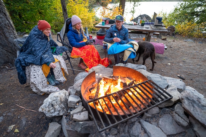 Three members of the Switchback Travel crew sit around a campfire and roast marshmallows