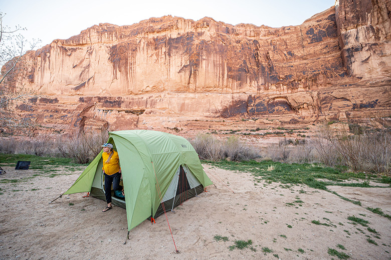 A camper pitches a spacious tent against a desert background of sheer, red rock walls. 