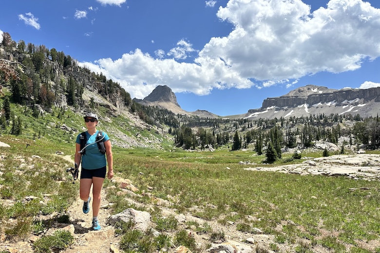 A woman hiking up a backpacking trail with mountain views behind her