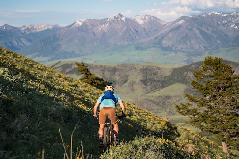 A man riding away from us on a trail with large mountains in the background