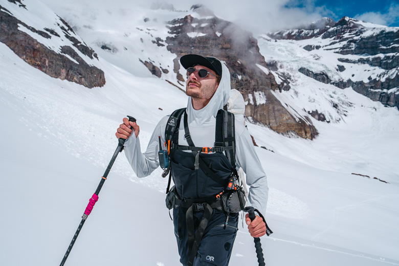 A man wearing a baselayer and ski bibs ski tours with poles in a snowy mountain range