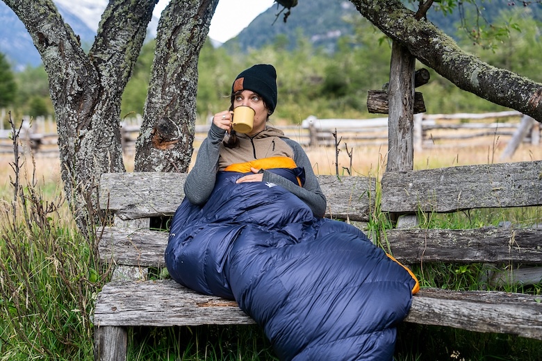 A woman enjoying a cup of coffee while tucked inside a sleeping bag