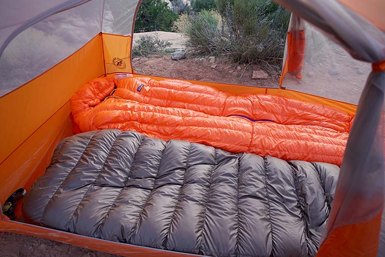 A sleeping bag and quilt are compared side-by-side in a tent. 