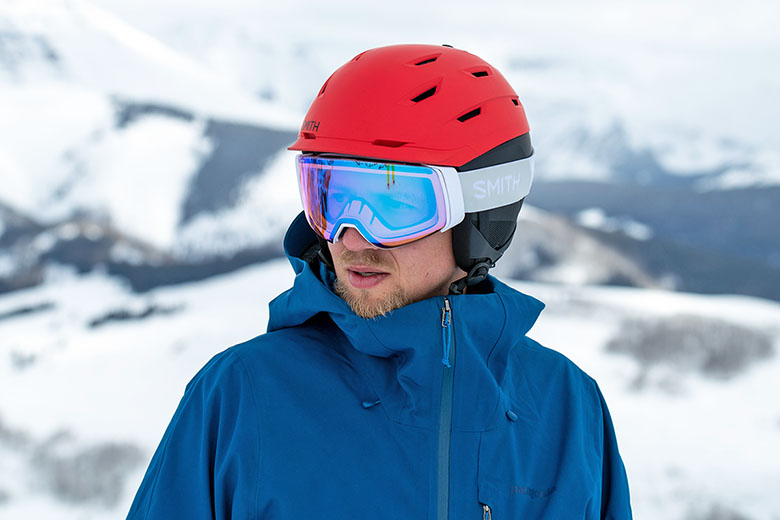 A skier wears a bright red ski helmet on a snowy mountain top.