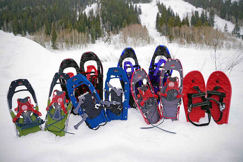 Five pairs of different colored snowshoes are displayed in the snow.