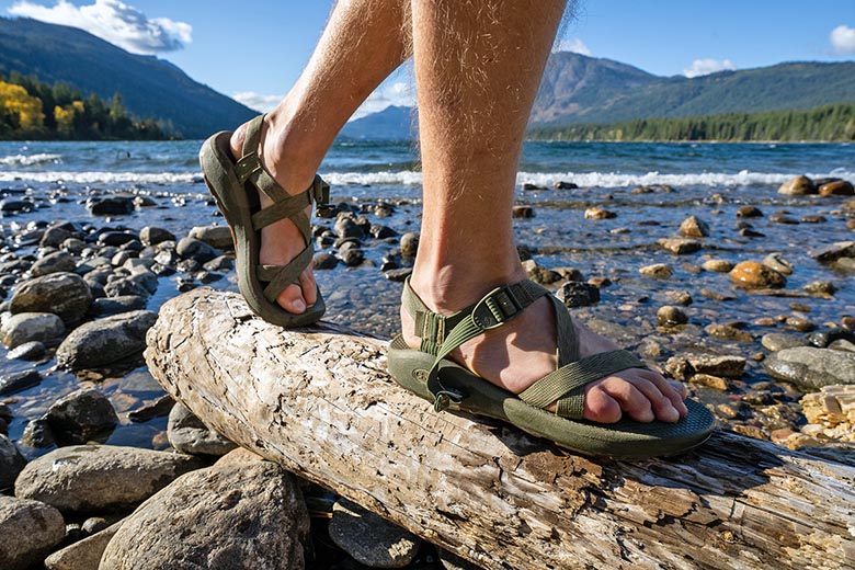 A person hiking over a log on a beach in Chaco sandals