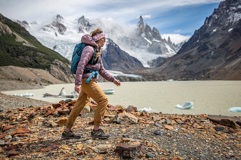 A woman hikes in front of mountains in Patagonia wearing a synthetic jacket