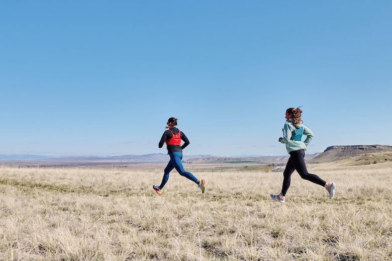 Two runners cross a field wearing running packs.