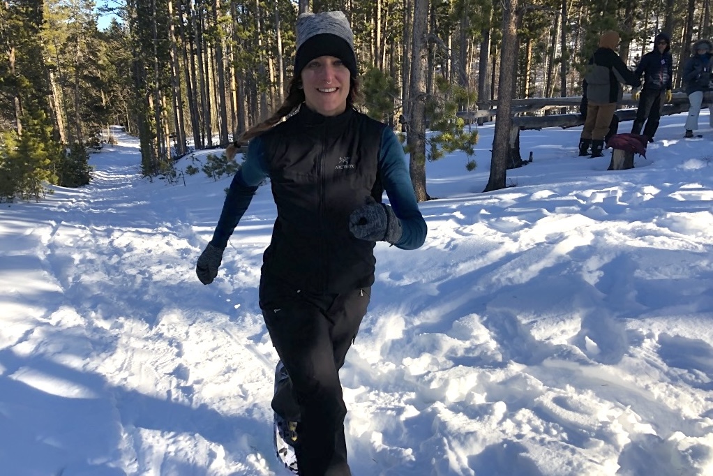 A woman with a smile running in the forests of Colorado.