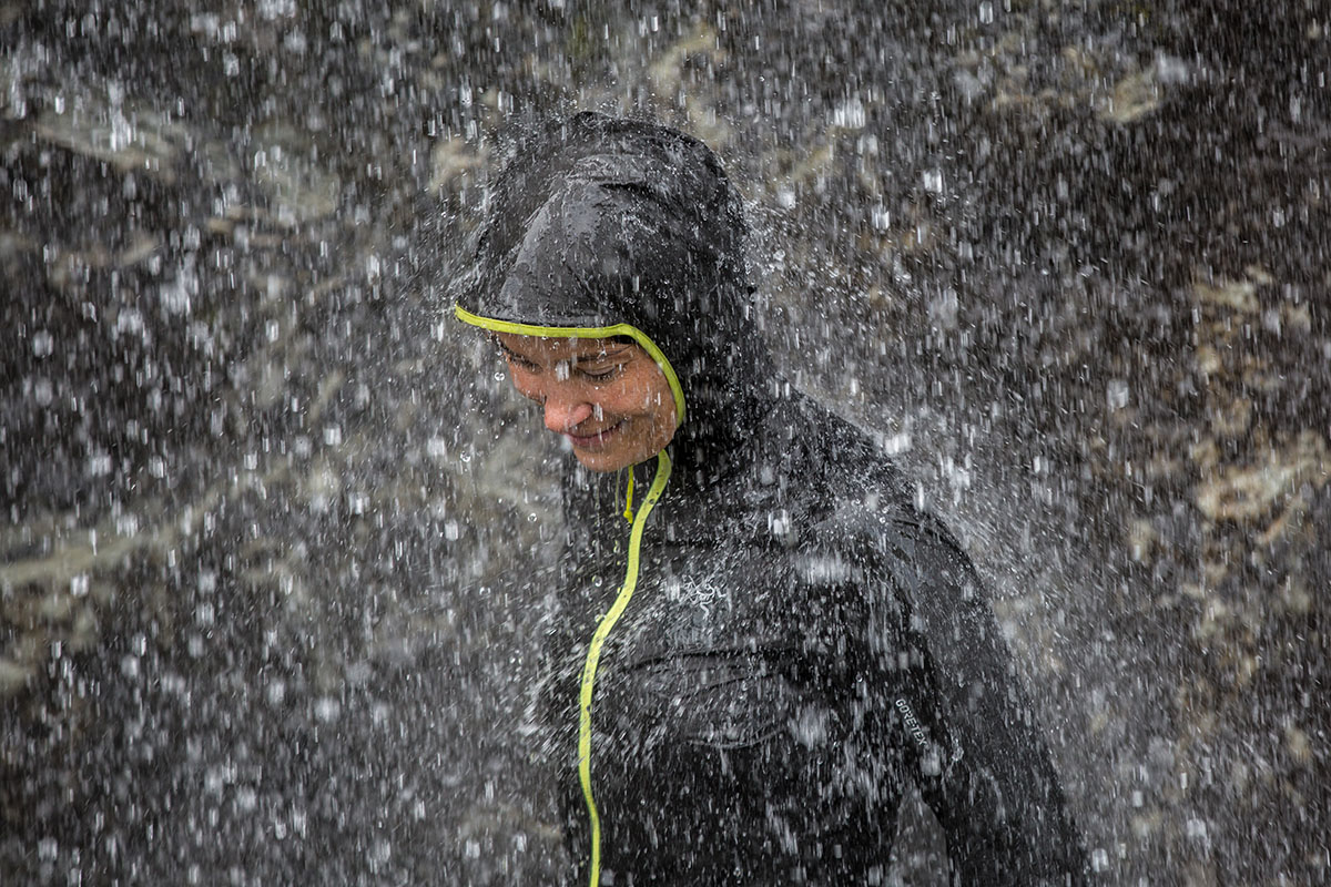 A woman stands under a waterfall to test the Arc'teryx Norvan SL Hoody
