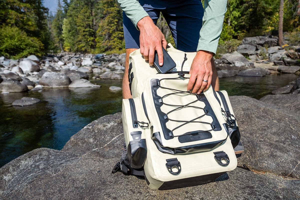 A hiker showcases the exterior zipper pocket on their backpack cooler. 