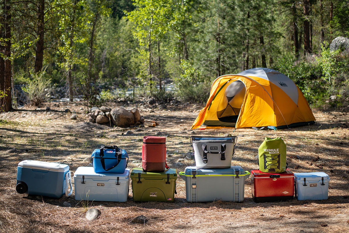 Ten coolers stacked up side-by-side at a campsite, showing off their sizes and colors.