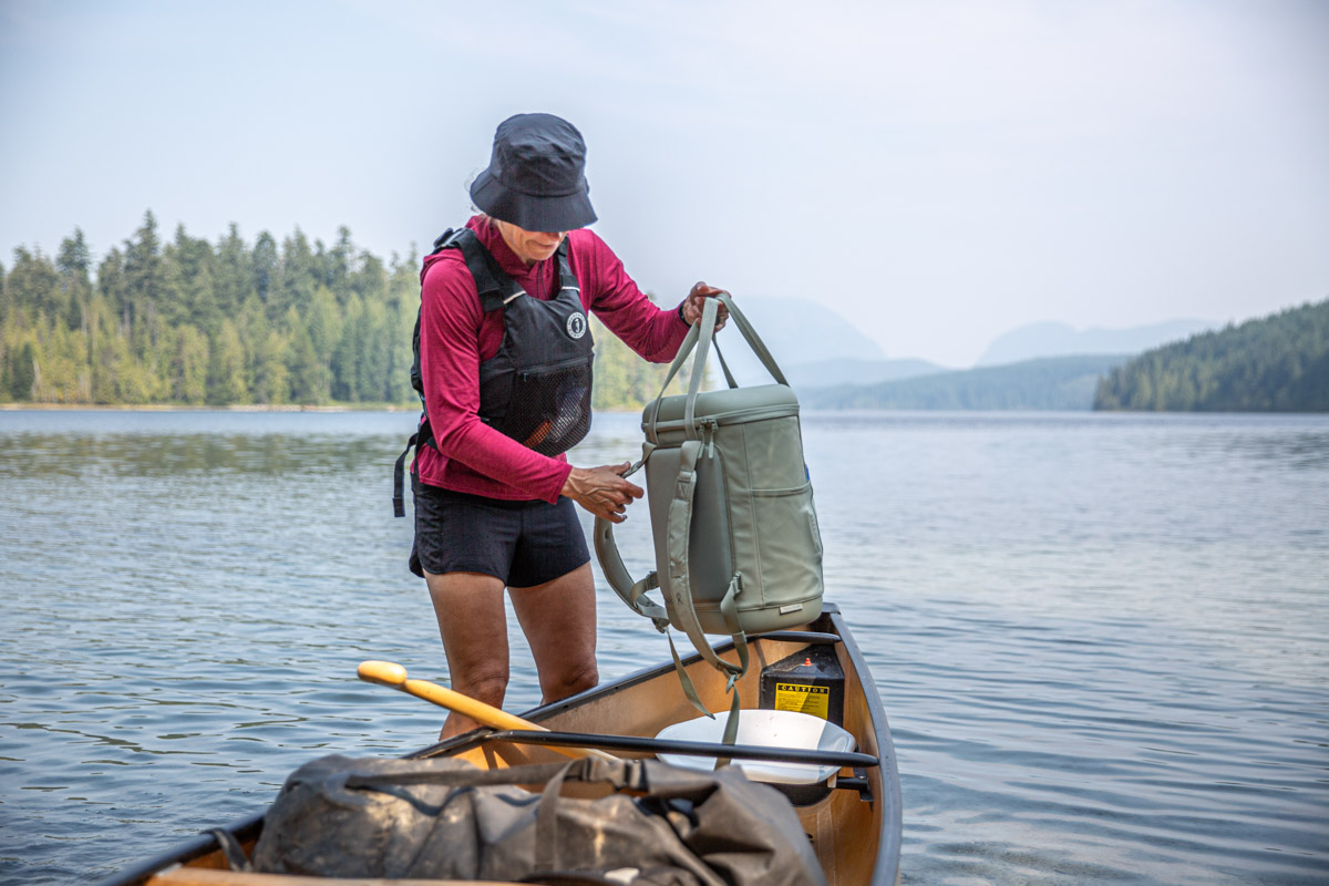 A woman carrying a backpack cooler out of a canoe