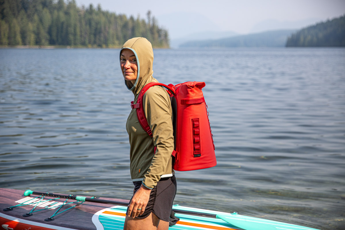 A woman puts her paddleboard out in the water, and carries her backpack cooler with her.