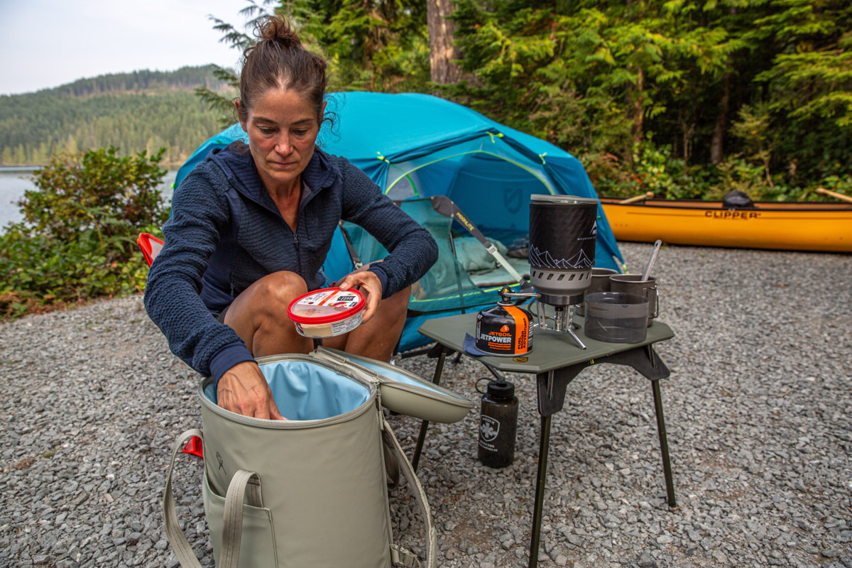 A camper unloads snacks and picnic supplies from her backpack cooler.
