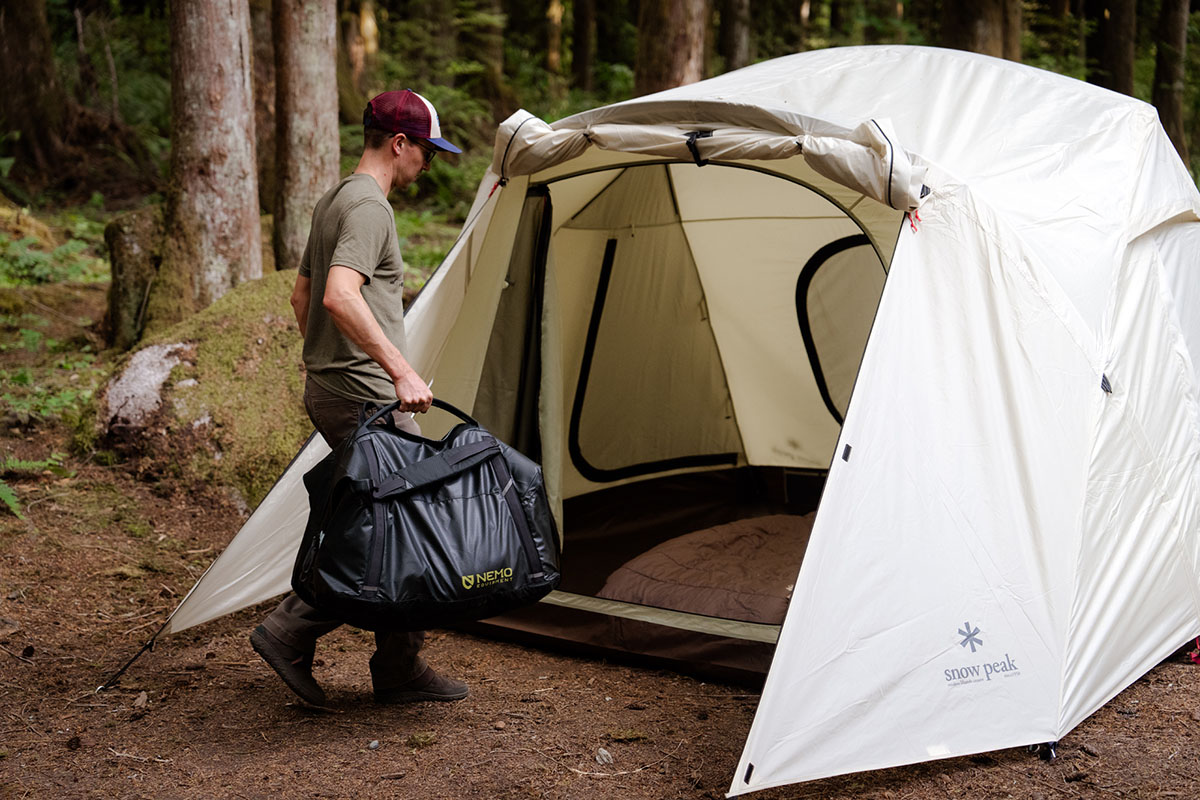 A camper brings his bags into his camping tent to set up his sleeping space.
