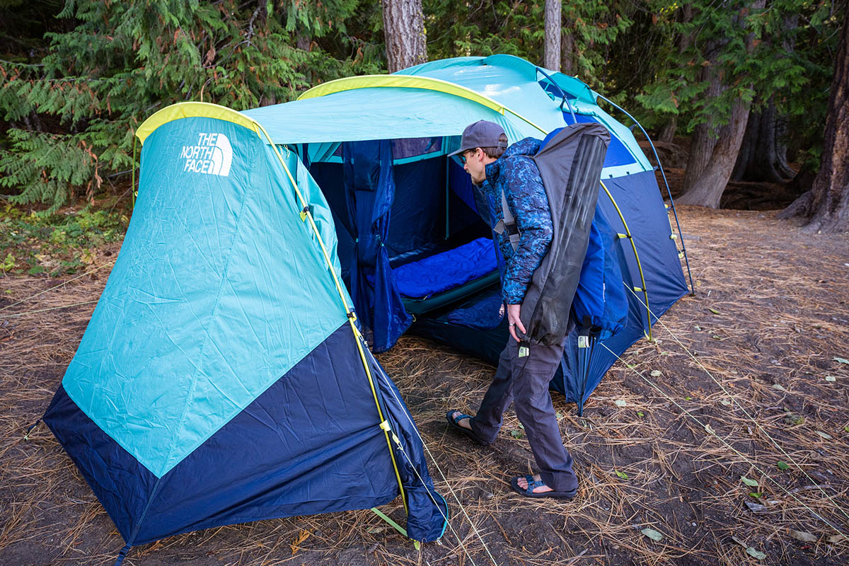 A man steps into a spacious vestibule in a camping tent.