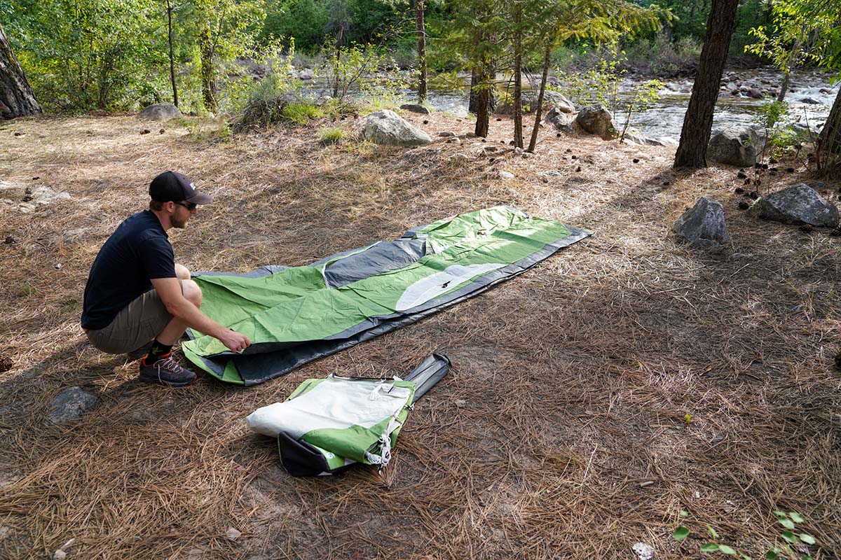 A camper folds their tent down and rolls it, so it can fit in a backpack for carrying.