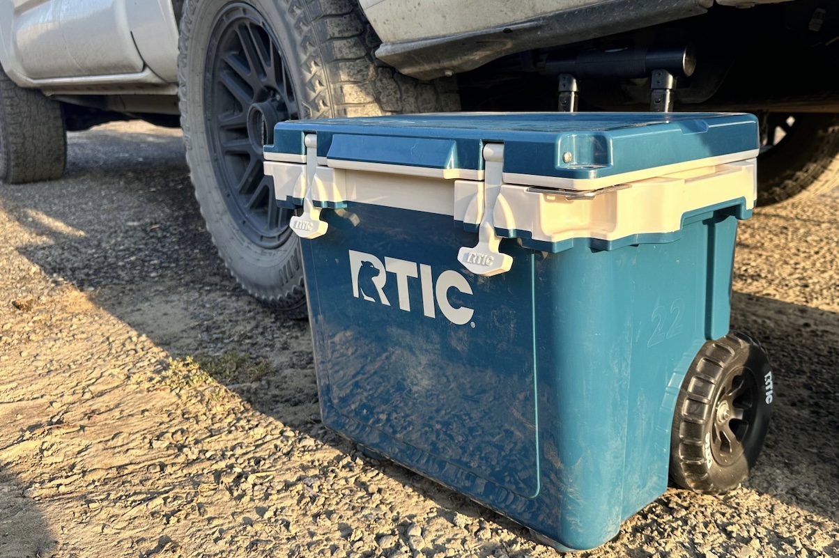 A dirty and muddy cooler is ready to be packed into a truck for camping.