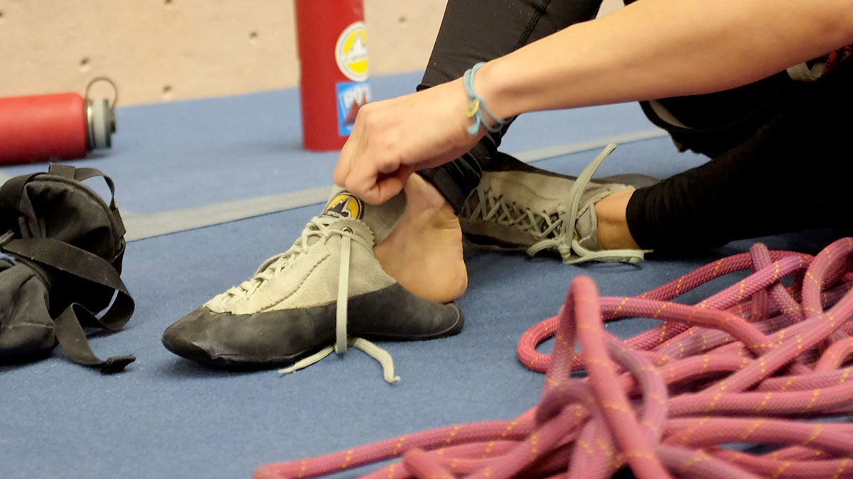 A hand pulling a pair of climbing shoes on at the gym