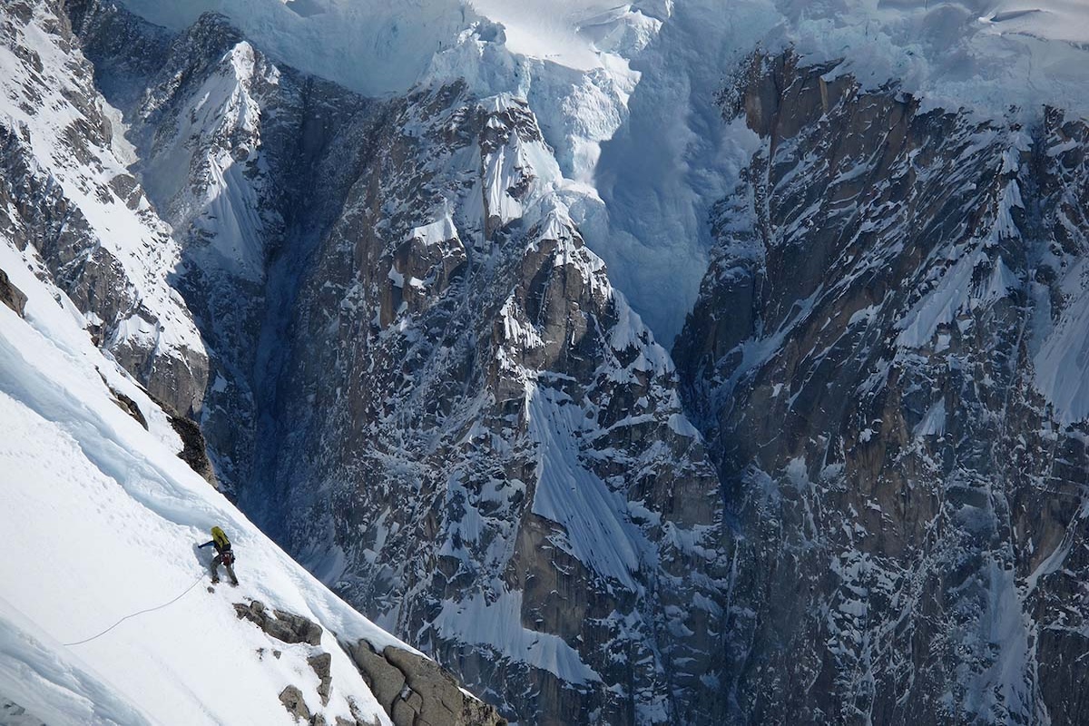 A man climbs a steep face on a snow-covered mountain peak.