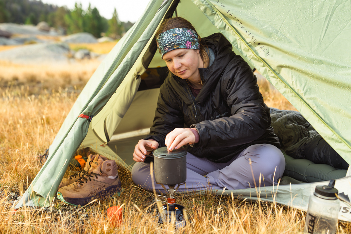 A woman using a backpacking stove in the vestibule of a budget backpacking tent