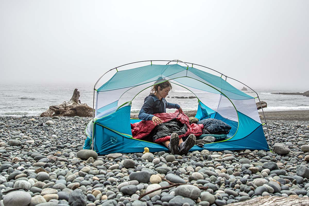 A woman preparing a sleeping bag inside a blue budget backpacking tent