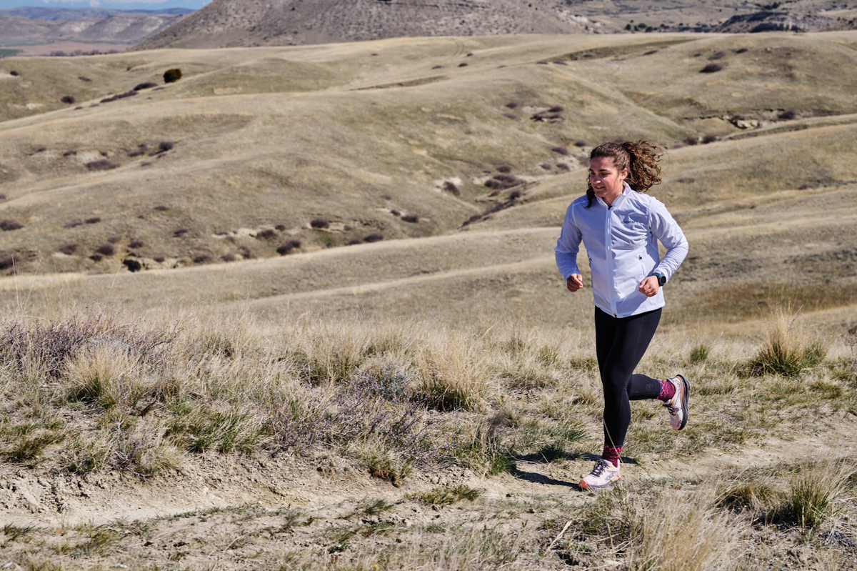 A woman running up a hilly trail wearing a fitness watch