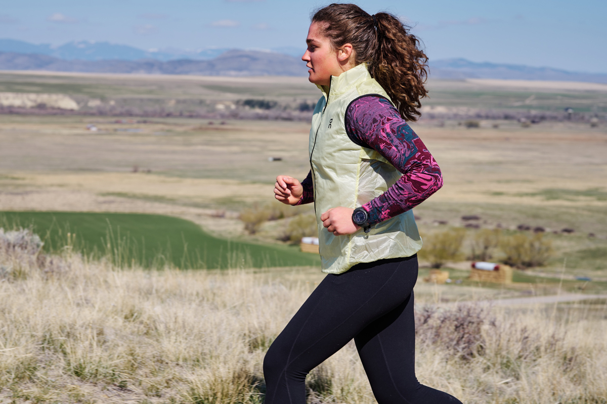 A woman running on a grassy trail while wearing a GPS watch
