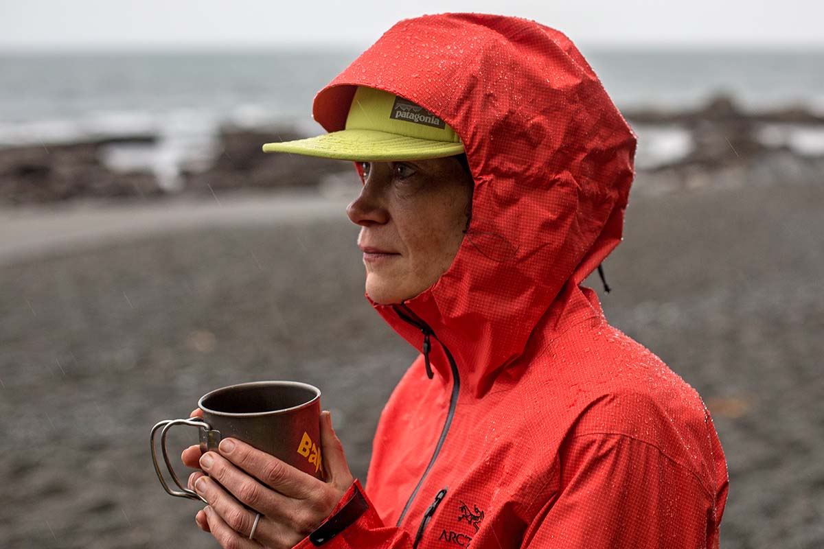 A woman wearing the Arc'teryx Alpha SL Anorak hardshel jacket while drinking from a cup