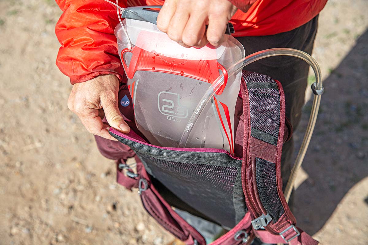 A hand pulling a hydration reservoir out of a red hydration backpack