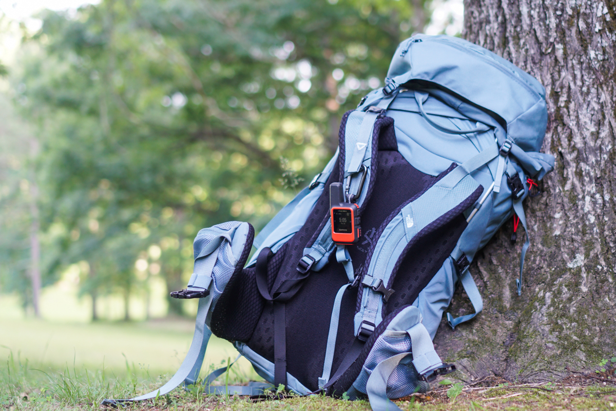 The inReach Mini 2 clipped to a backpack that leans against a tree