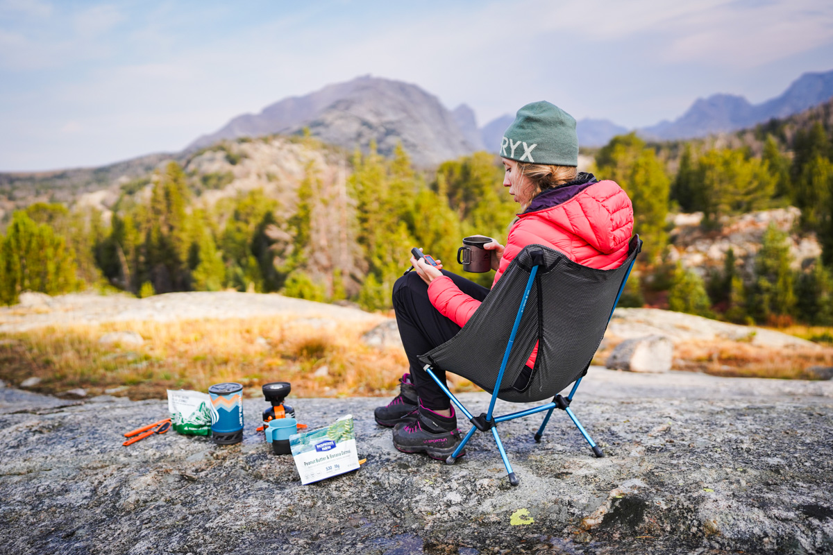 A woman sits in a chair out in the forest and consults a Garmin device in her lap