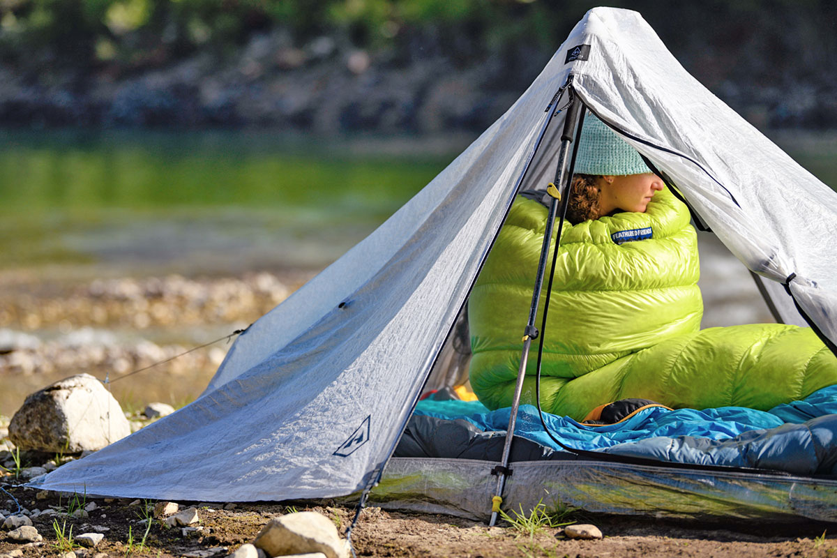 A camper is cocooned in a bright green sleeping bag under their tent.