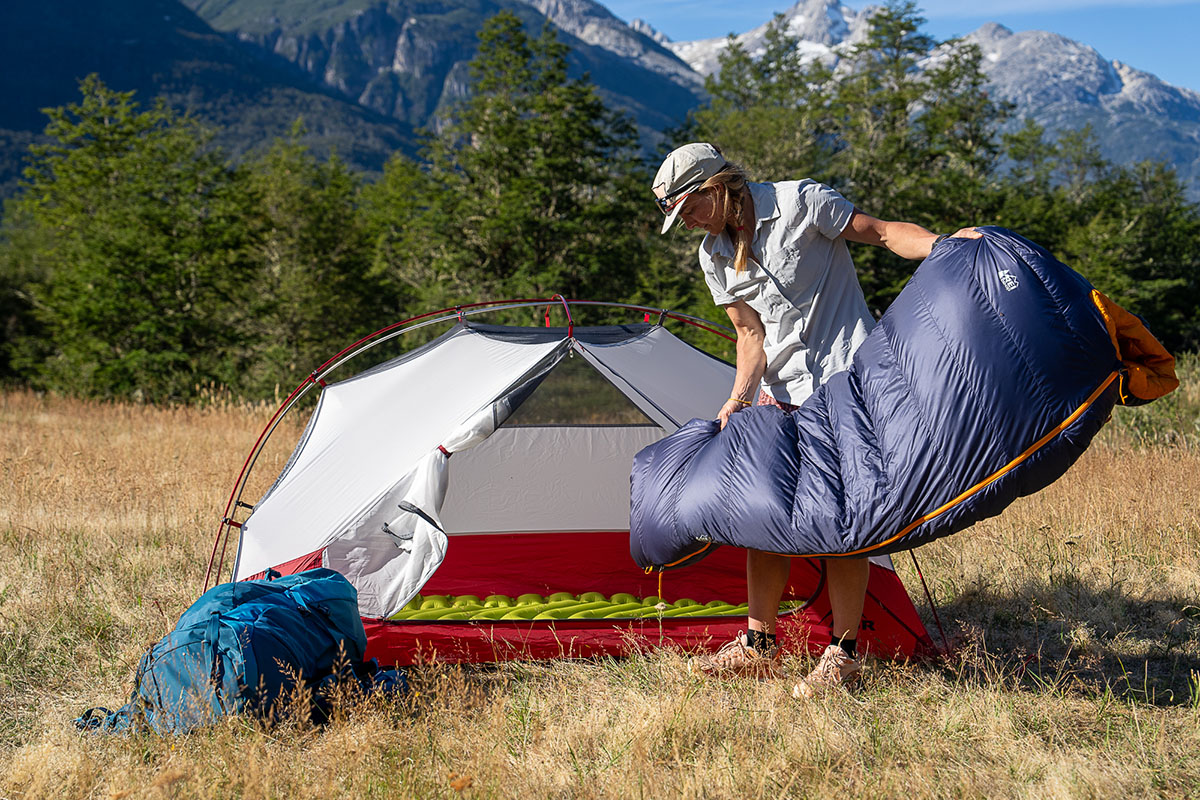 A camper tosses their sleeping bag into their tent. 
