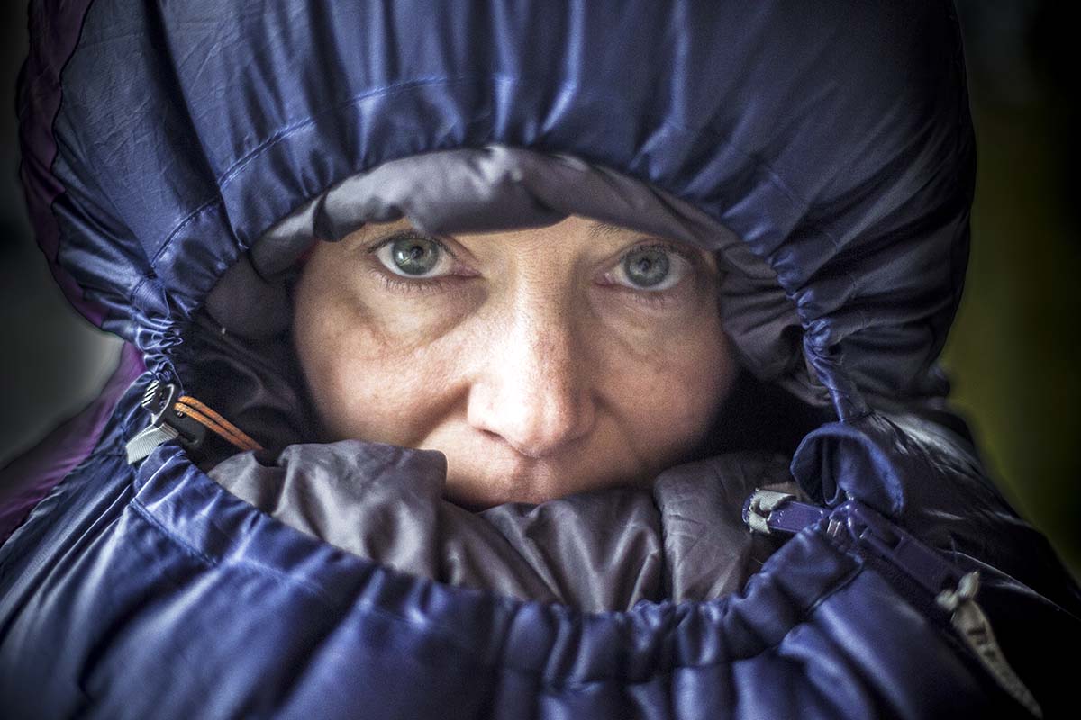 A camper has pulled the hood on their sleeping bag all the way around their face.