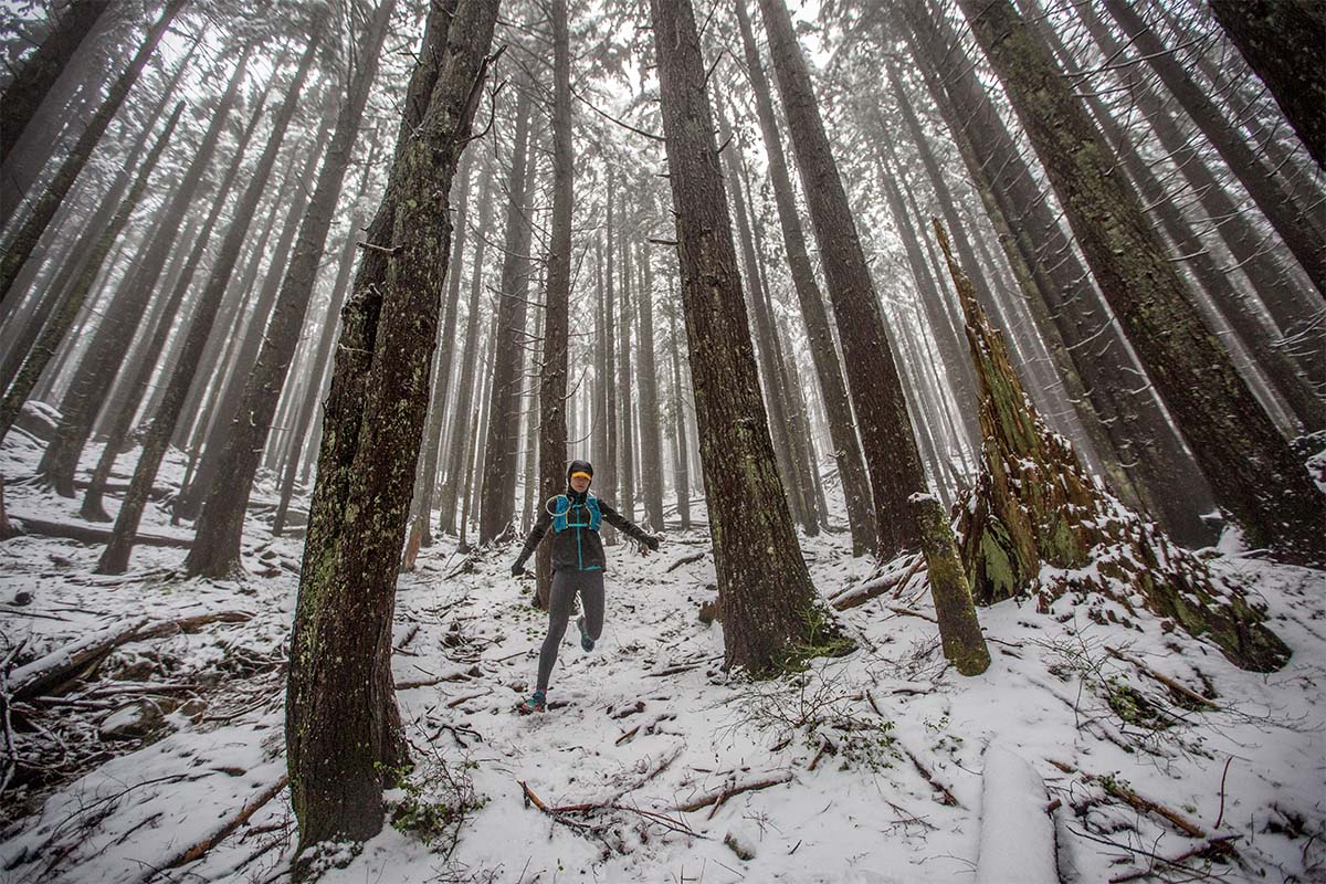 A trail runner runs downhill in a frosty, overcast forest.