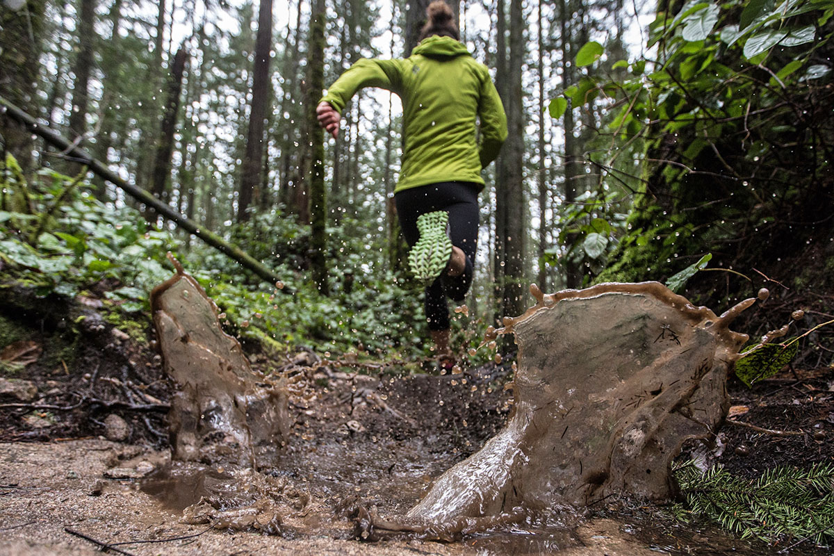 A woman trail runs in a wet, green forest, stomping through puddles as she goes.